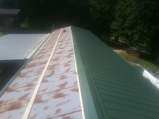 Old rusted panels beside newly installed green metal roofing — Wind Damage Roof Repair by Roofing Brothers in Milan